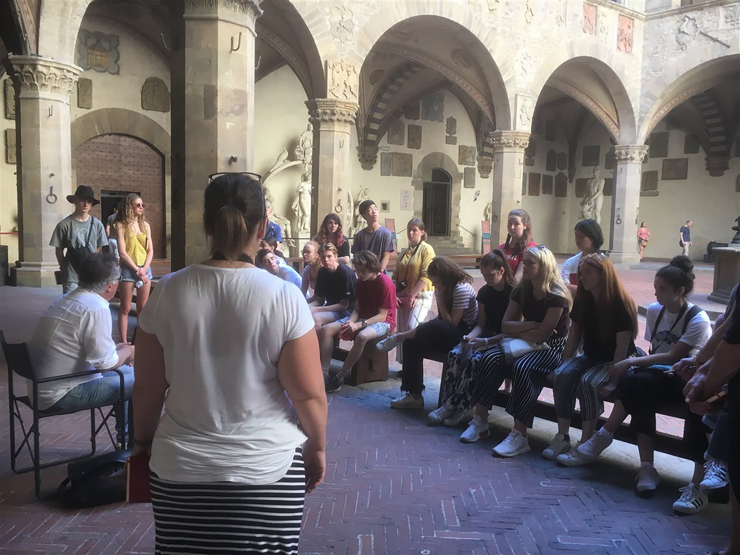 Students sitting on benches, listening to an art teacher during an art tour in Florence