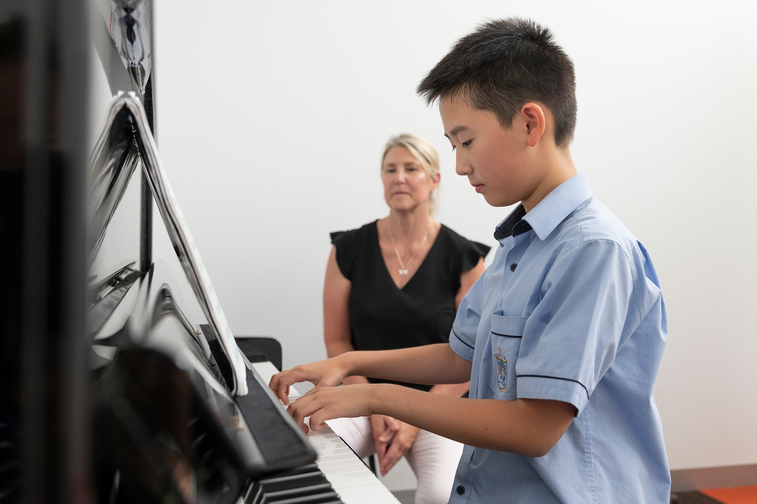 Young male student playing the piano with his teacher assisting him