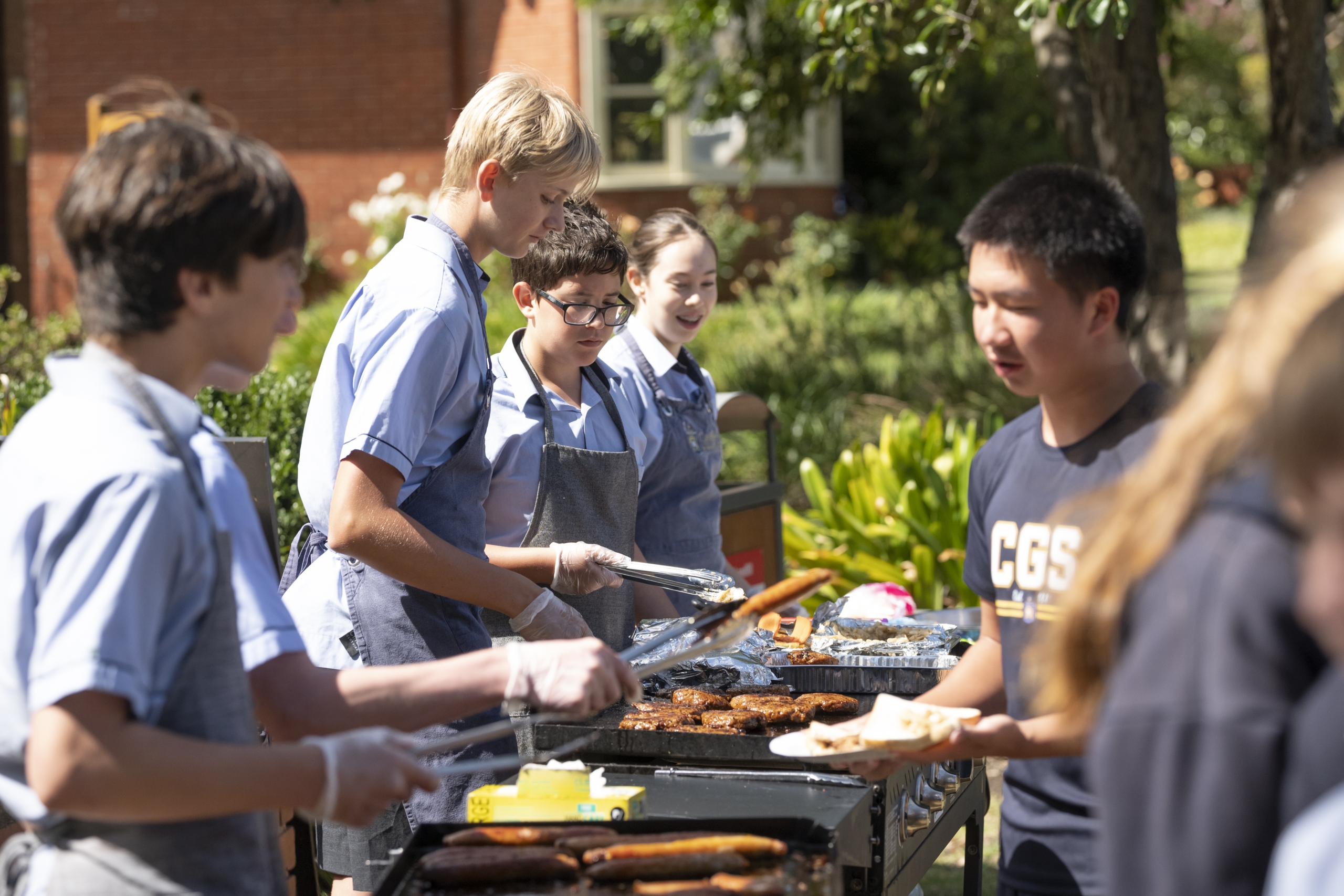 Students gathered around a grill, engaged in community service on the Caulfield Campus