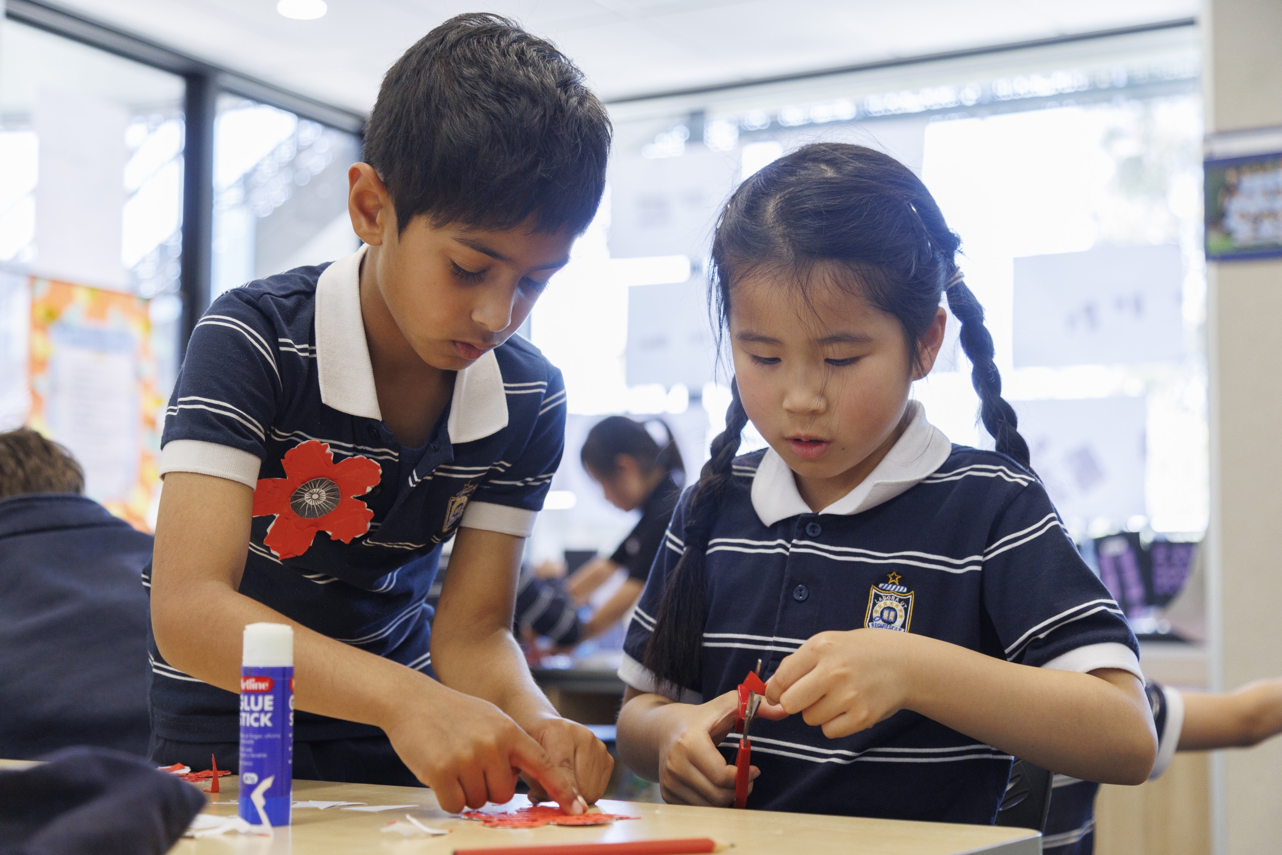 In a classroom, two junior school children are engaged in creative craft projects