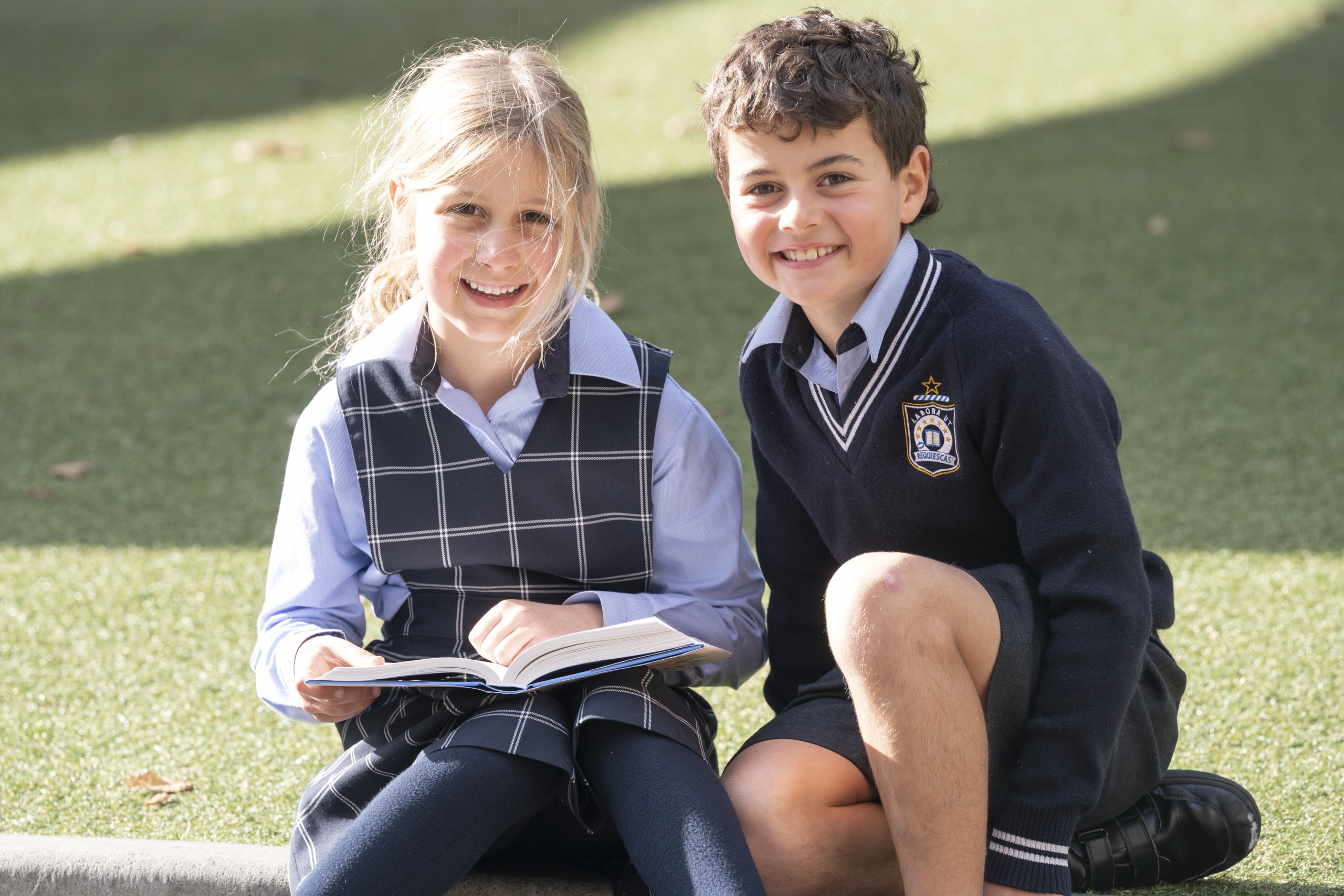 Two junior school students sitting on the grass and reading a book